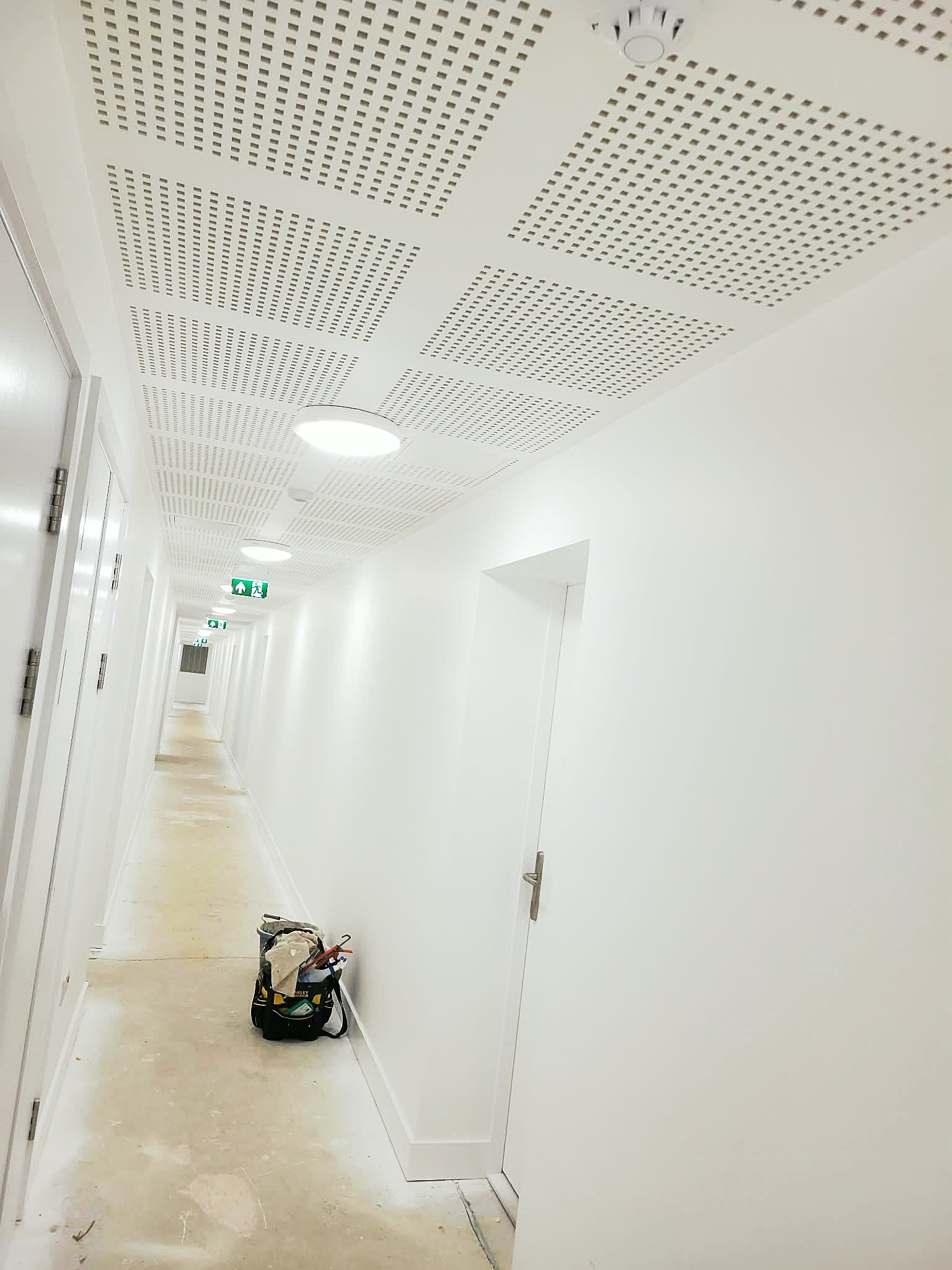 Long commercial corridor freshly painted in white, with perforated acoustic ceiling and floor protection down