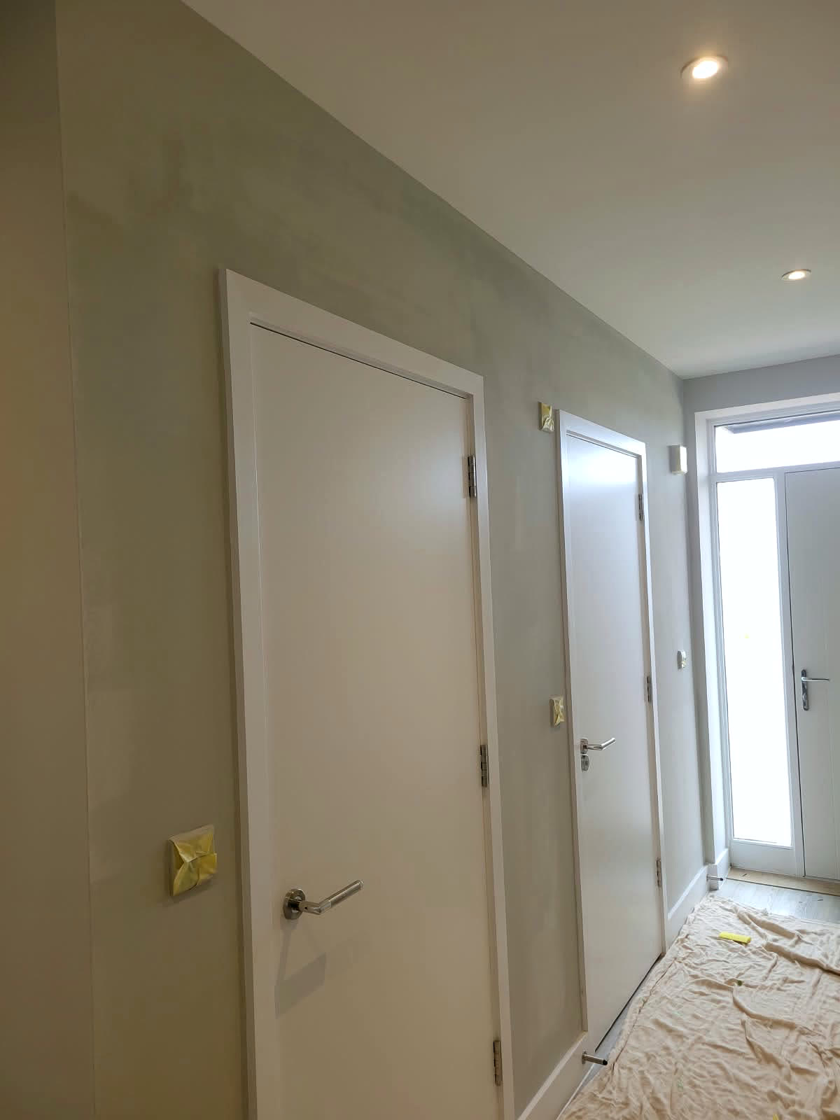 New-build hallway with walls painted and white doors finished, floor protected with sheets
